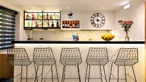A bar area with a marble countertop, black wire mesh chairs, a clock, and a variety of bottles and glasses on shelves. - Ideon Hotel (Chania)