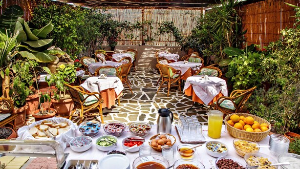 An outdoor dining area with tables set for breakfast, surrounded by potted plants and a bamboo backdrop. - Ideon Hotel (Chania)