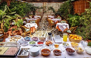 An outdoor dining area with tables set for breakfast, surrounded by potted plants and a bamboo backdrop. - Ideon Hotel (Chania)