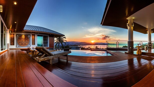 A luxurious outdoor area with a wooden deck, a pool, and a view of the sunset over the ocean. - NB Villa Vimana (Koh Samui)