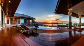 A luxurious outdoor area with a wooden deck, a pool, and a view of the sunset over the ocean. - NB Villa Vimana (Koh Samui)