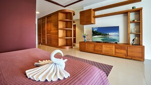 A hotel room with a large bed, a wooden cabinet with shelves, a flat-screen TV, and a painting of a beach scene. - NB Villa Vimana (Koh Samui)