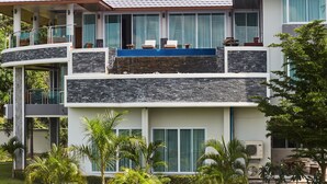 A multi-story hotel with a balcony on the second floor, large windows, and a stone facade. - NB Villa Vimana (Koh Samui)