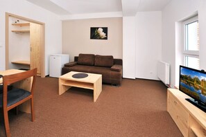 A compact living space with a brown sofa, a small wooden table, a white radiator, and a television on a wooden cabinet.