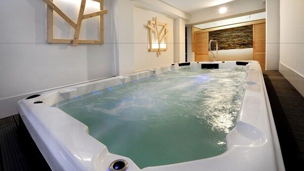 A large indoor hot tub with a wooden wall design and a stone wall in the background. - Apartmány Belveder (Vysoké Tatry)