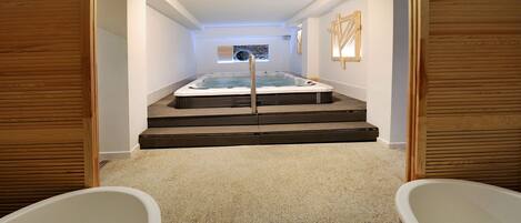 A spa area with a hot tub, a walk-in shower, and a wooden floor.