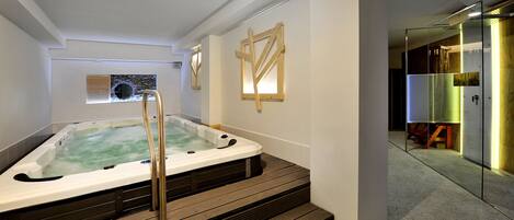 Un baño moderno con bañera de hidromasaje, escalones de madera y mampara de vidrio.