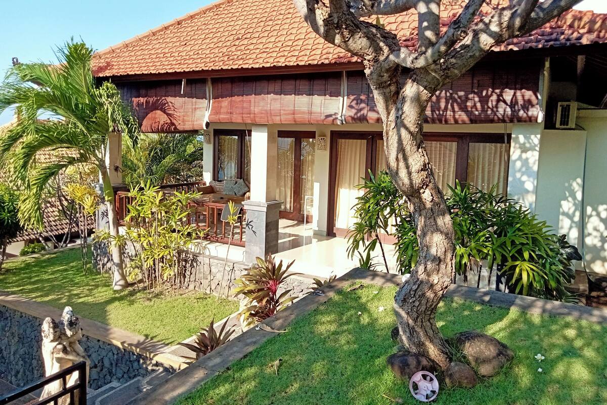 A house with a tiled roof, a covered patio, and a lawn with various plants.