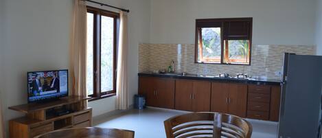 A spacious living area with a wooden dining set, a television, and a kitchen with wooden cabinets and a tiled backsplash.