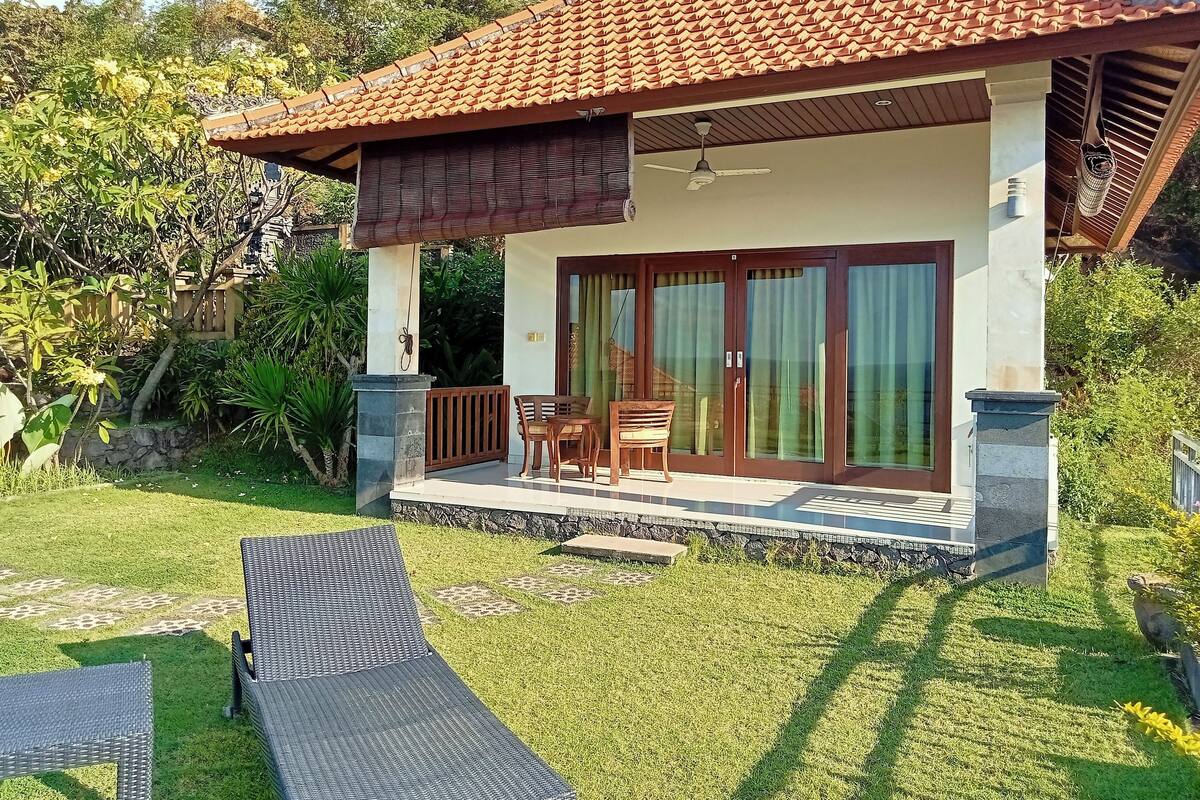 A house with a tiled roof, a covered porch with a table and chairs, and a grassy yard.