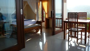 Un dormitorio con cama, un balcón con mesa y sillas, y vista al océano.