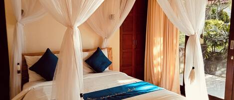 A bed with a canopy, a wooden door, and a view of greenery outside.