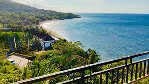 Vista costera con playa, un edificio pequeño y abundante vegetación.