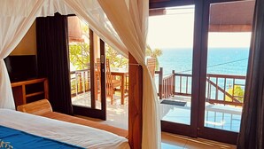 Un dormitorio con cama, televisión y balcón con vista al mar.