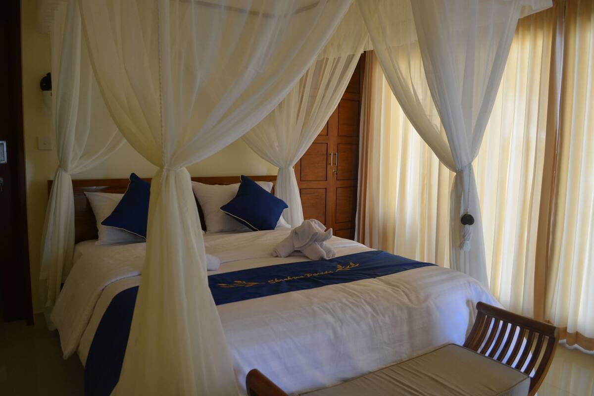 A bed with a canopy, pillows, a wooden headboard, a bedside table, and a chair.