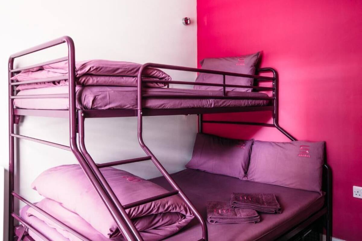 A bunk bed with purple bedding in a room with a pink wall.