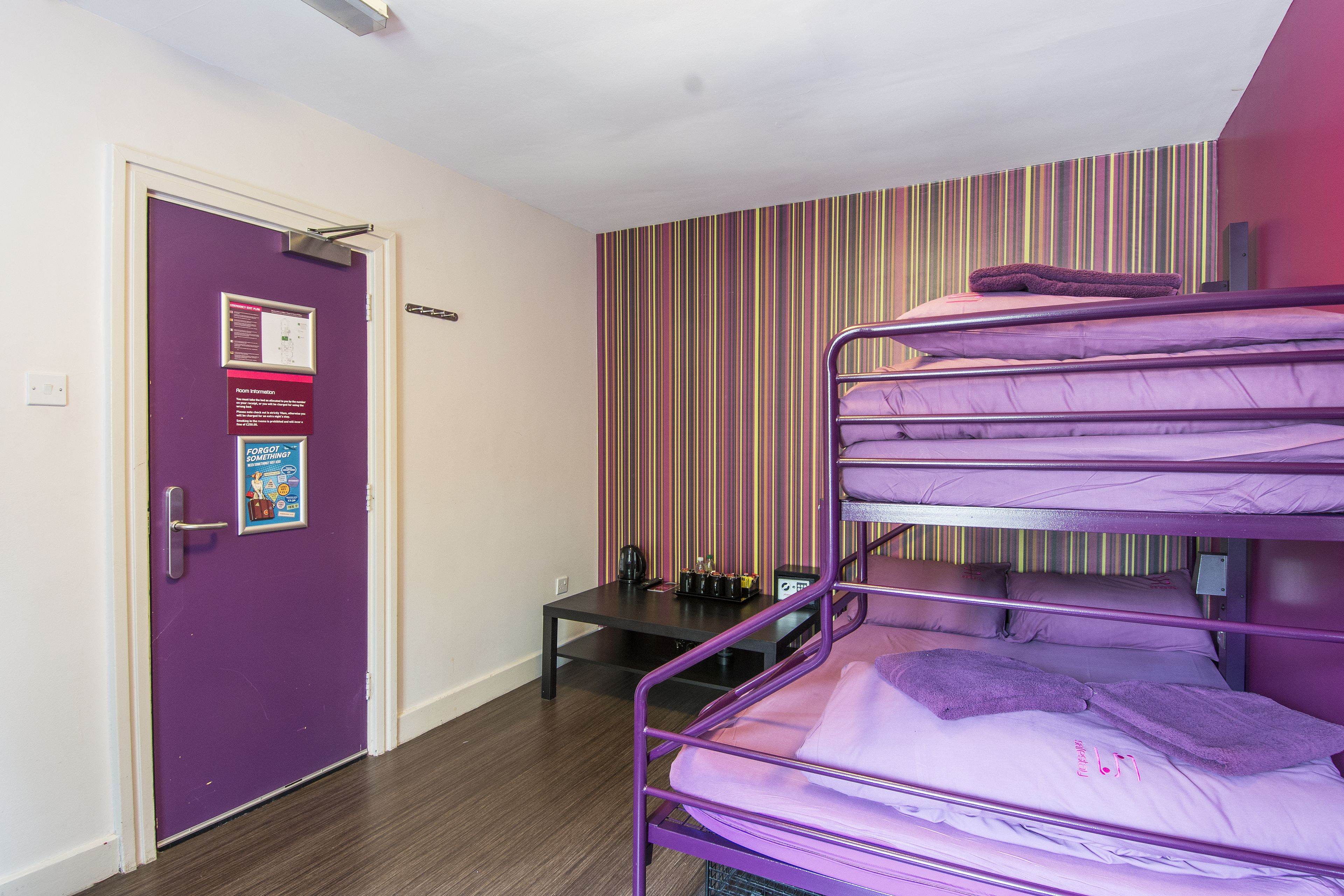 A dormitory room with bunk beds, a door with a notice, a striped wall, and a small table with items on it.