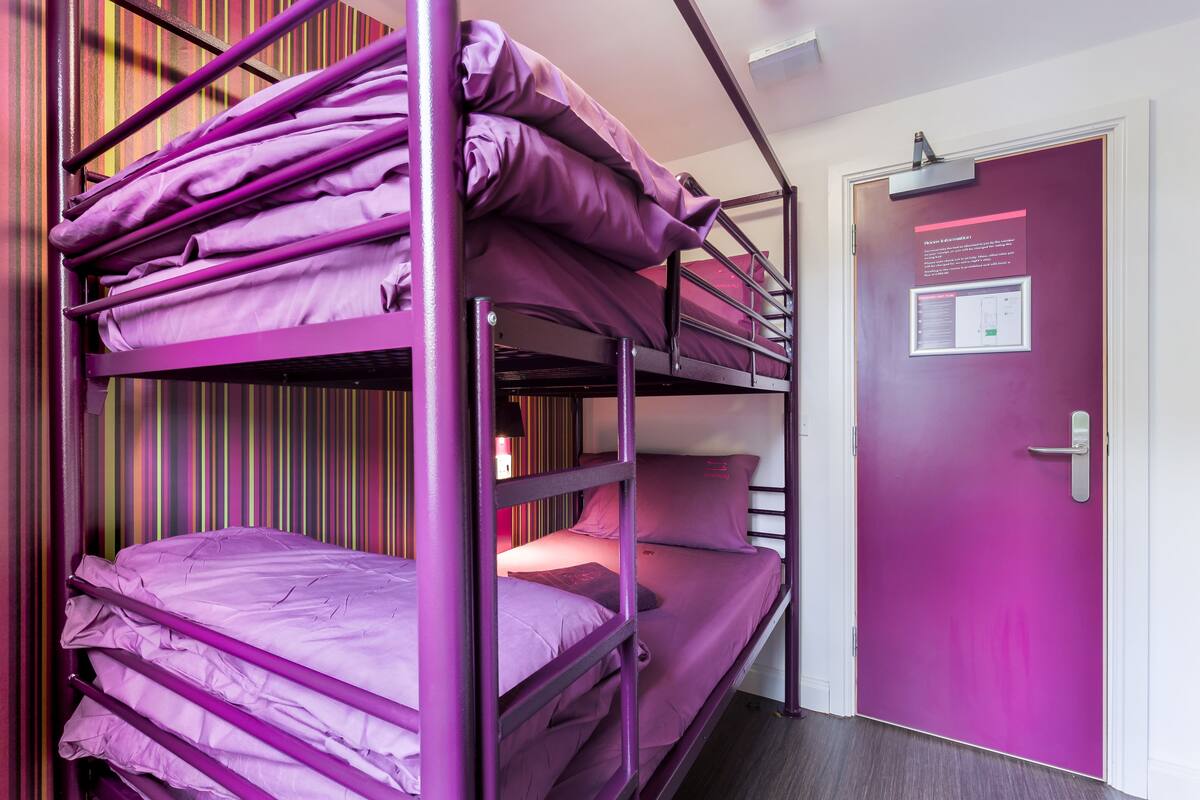 A bunk bed room with purple bedding and a door with a notice.