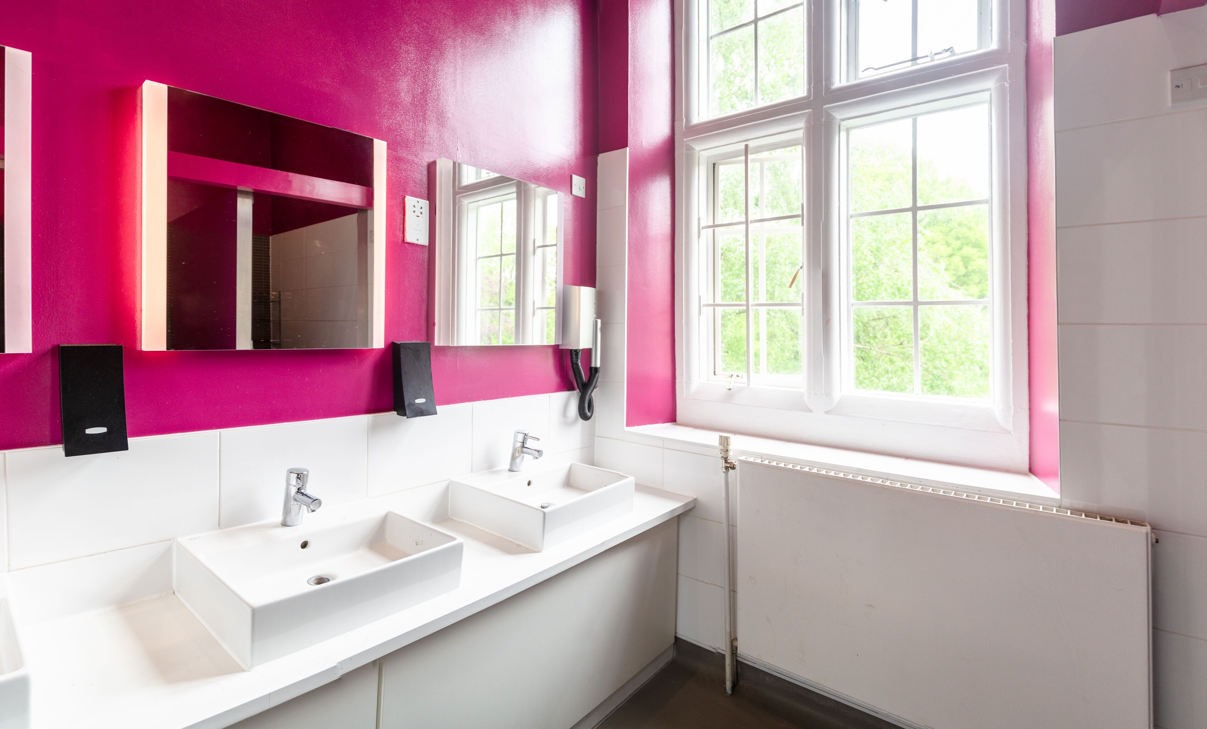 A modern bathroom with two sinks, a large mirror, and a window with a view of greenery.