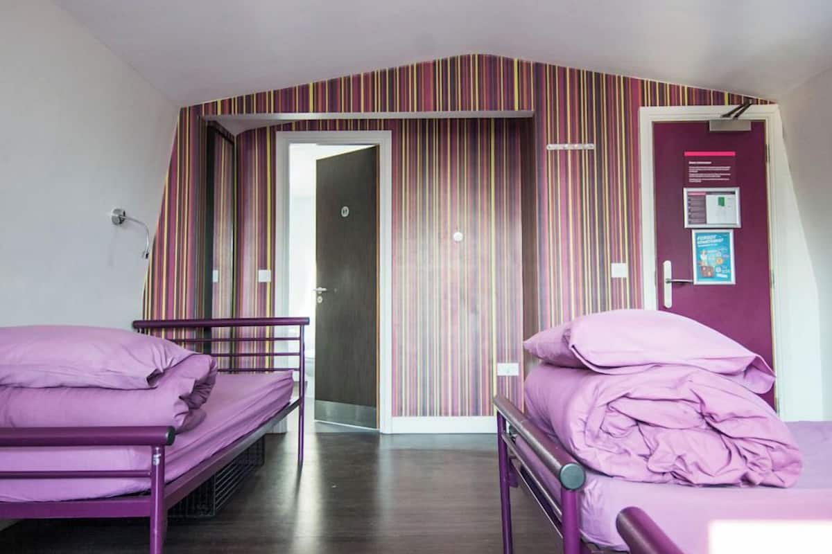 A room with two beds, a striped curtain, a door, and a wall-mounted light fixture.
