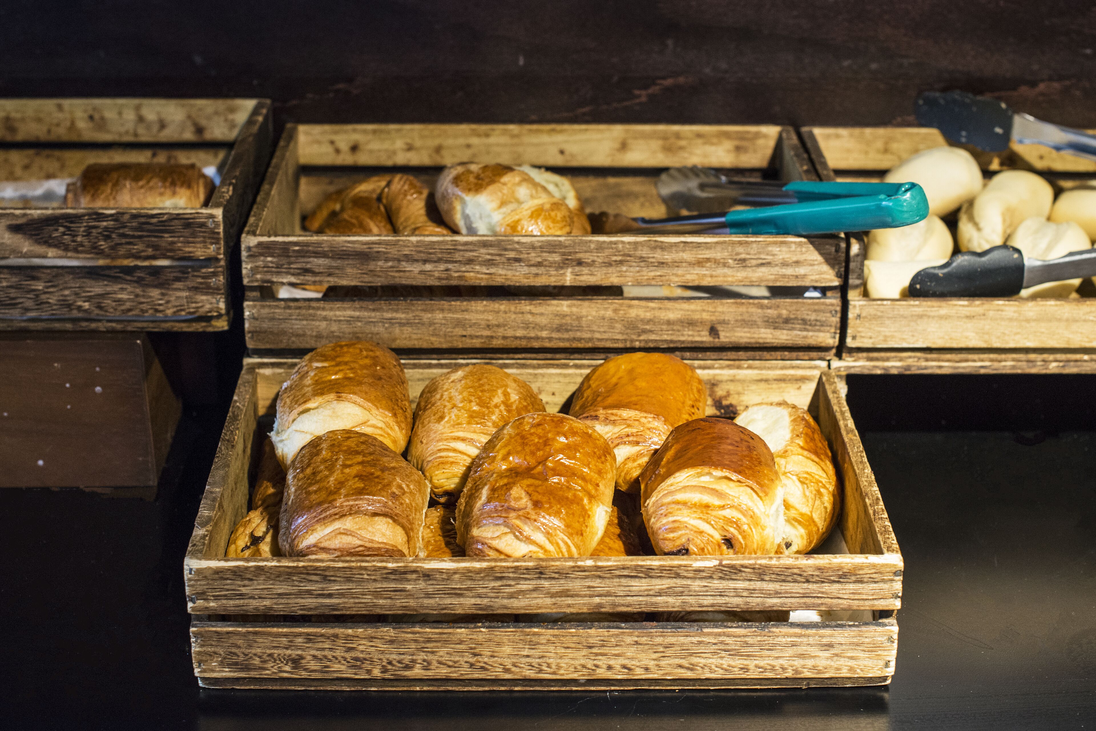 A wooden crate filled with various pastries, including croissants and bread rolls.