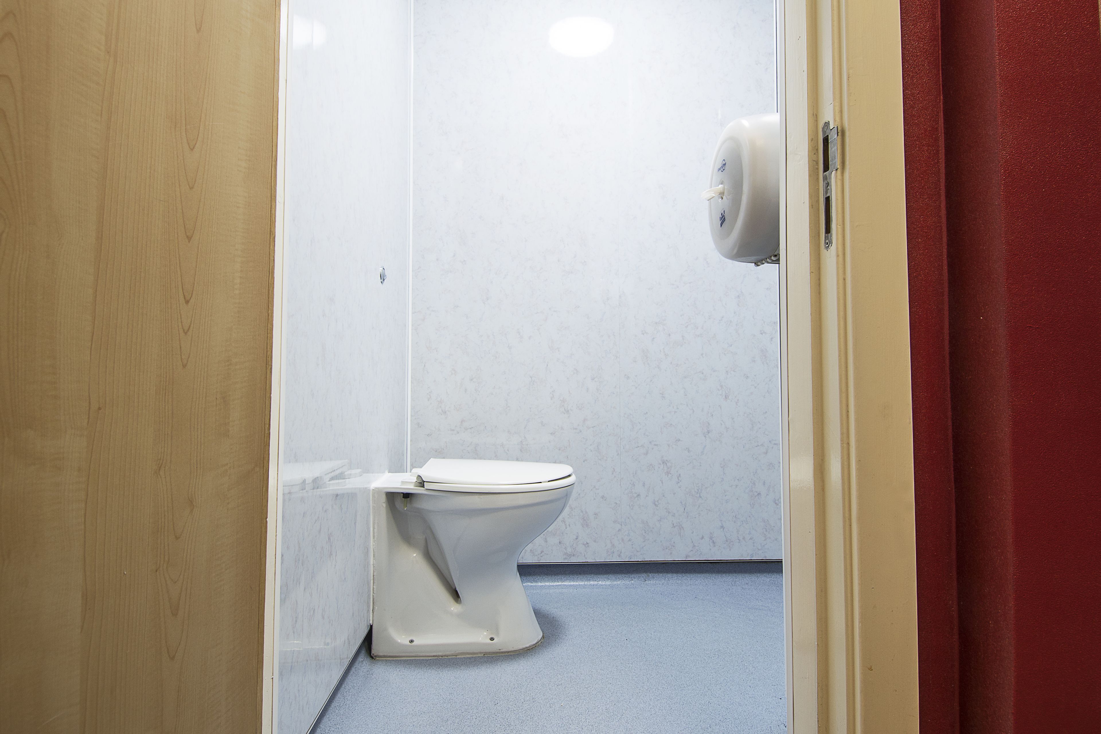 A small, compact bathroom with a white toilet, a marble wall, and a red curtain.