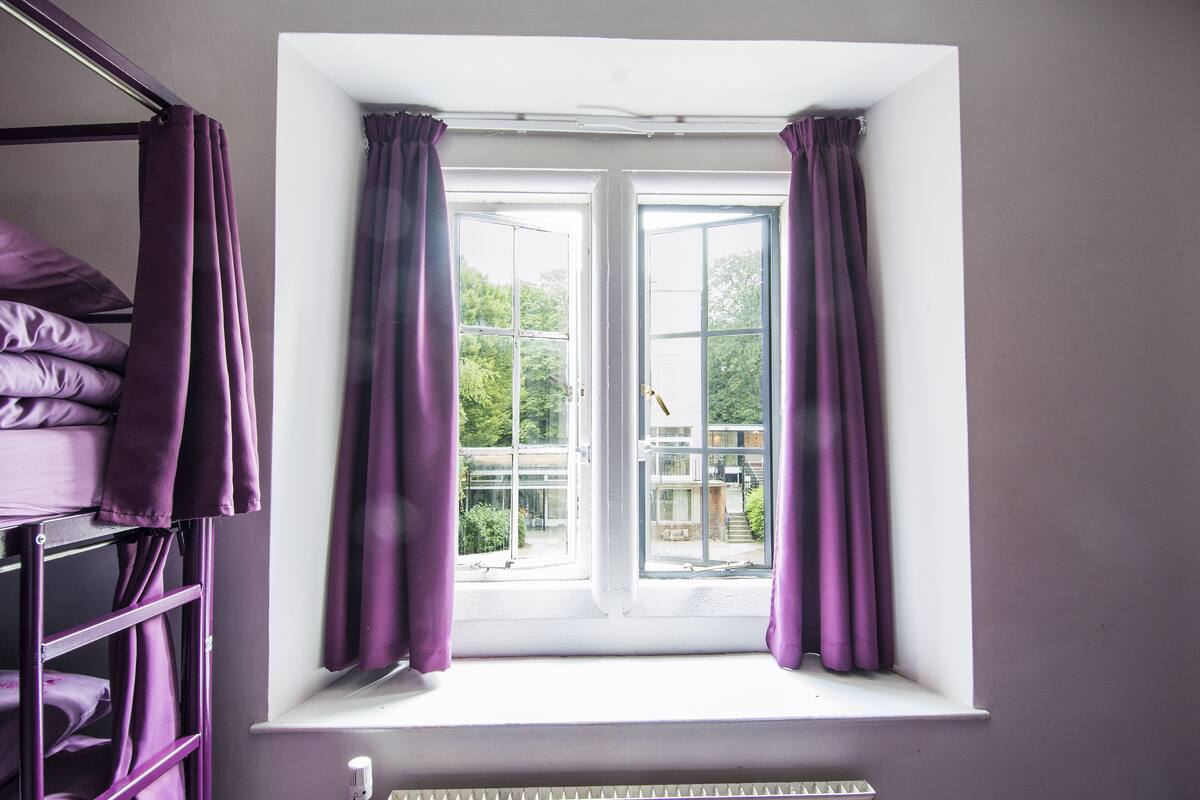 A window with purple curtains, a white radiator below, and a metal shelf to the left.