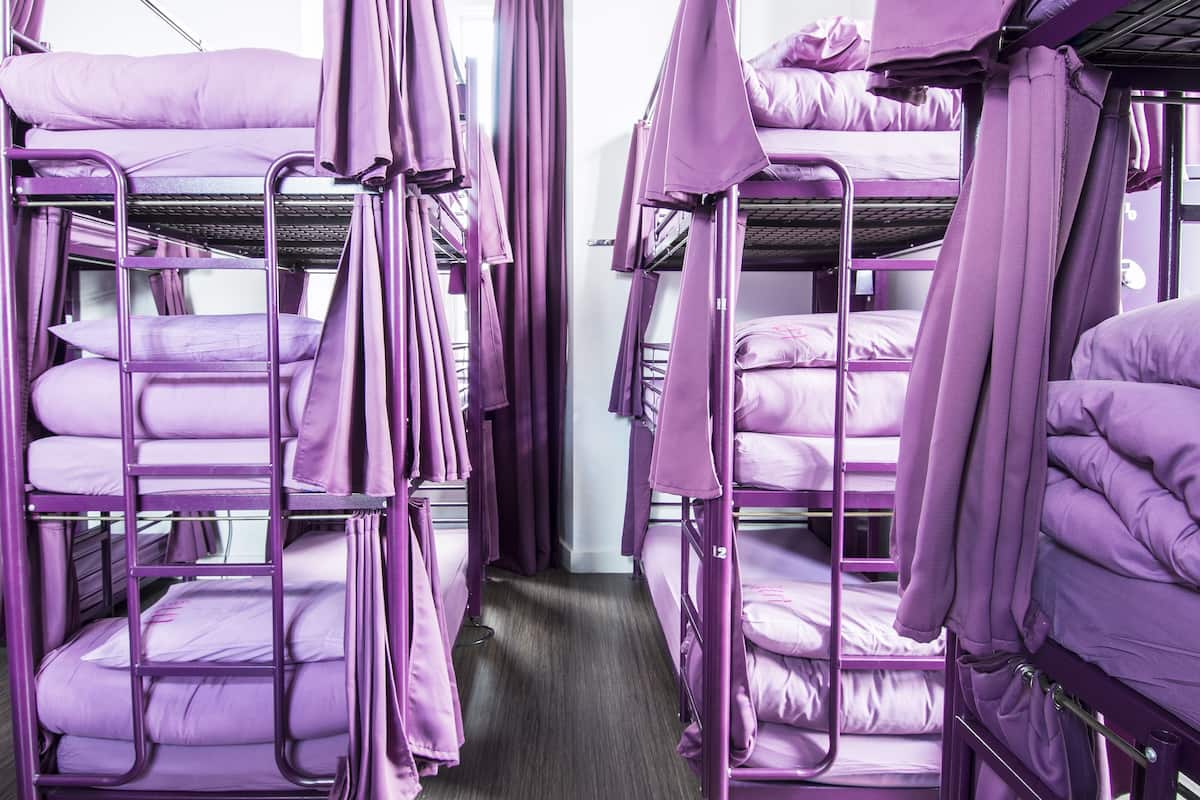 A row of bunk beds with purple bedding and curtains, arranged in a narrow corridor.