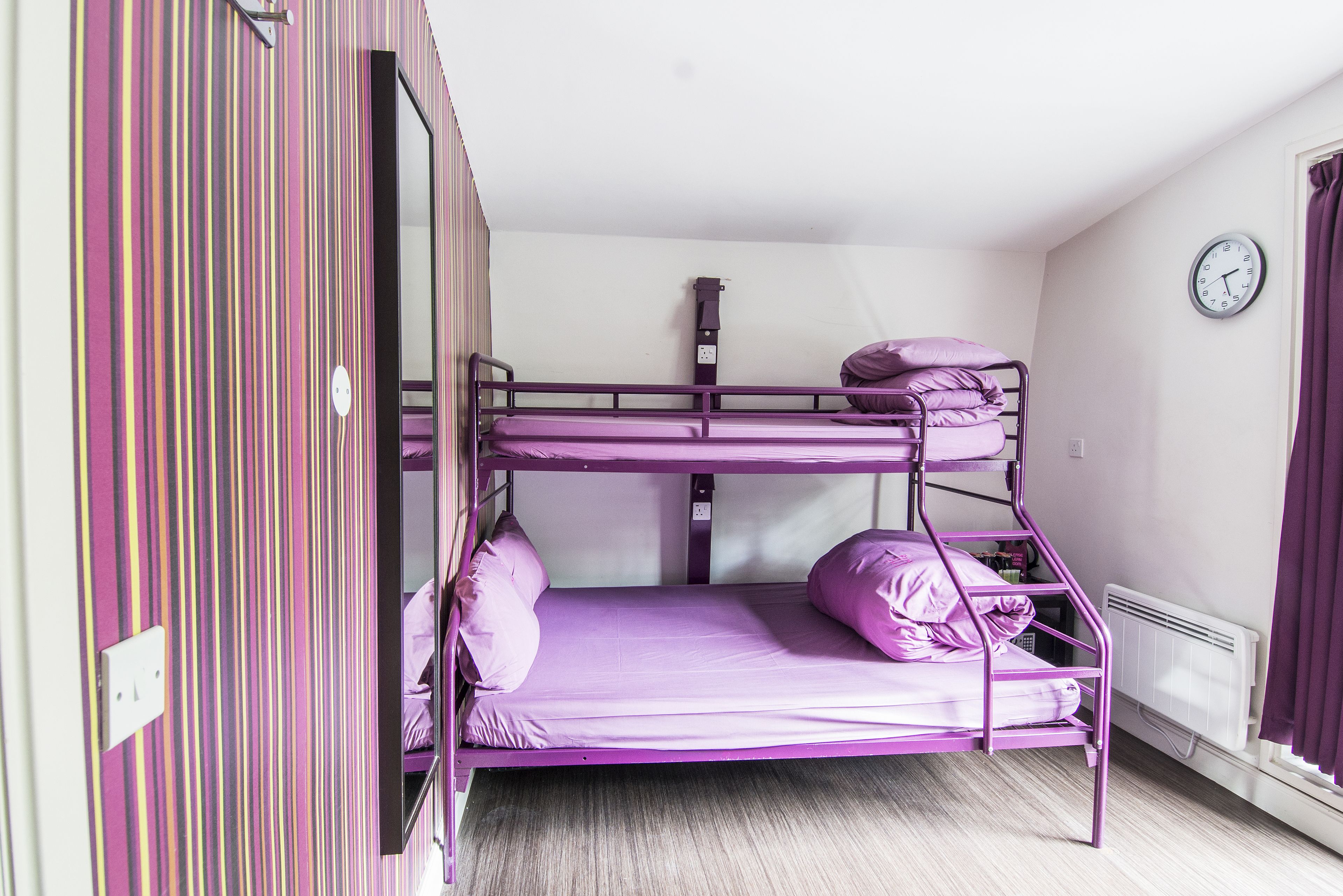 Habitación con literas de color morado, un reloj en la pared y un radiador.