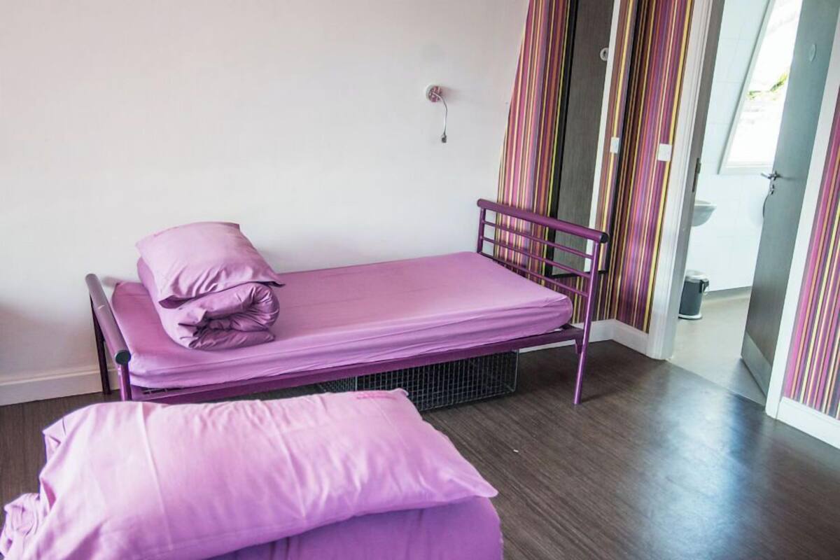A single bed with a metal frame and a mattress, a pillow, and a bedside table with a lamp.