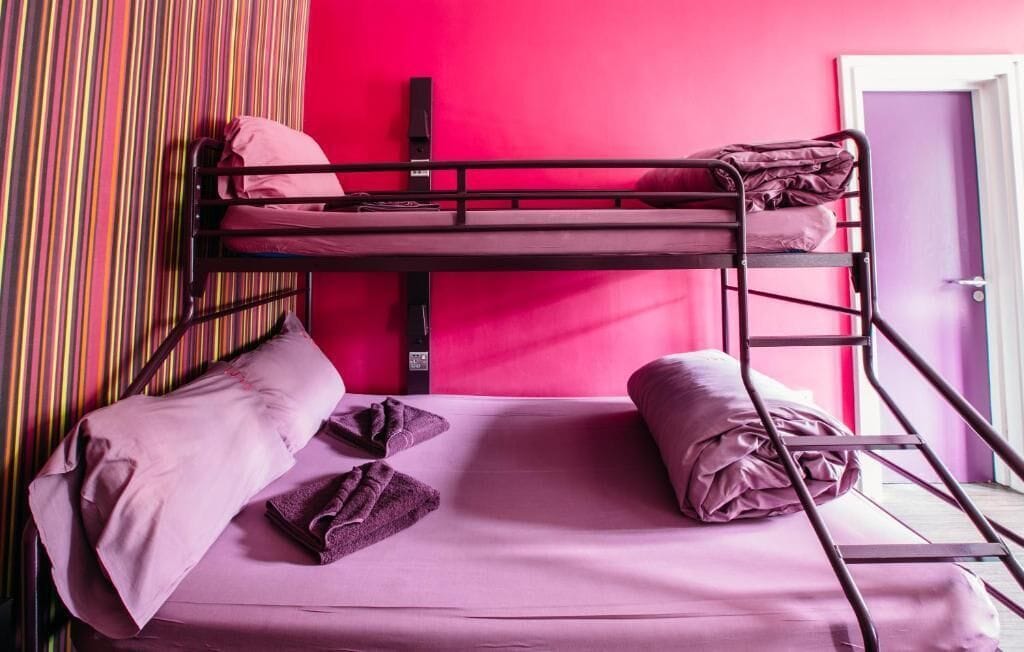 A bunk bed with a pink mattress and pillows, a striped curtain, and a door in the background.