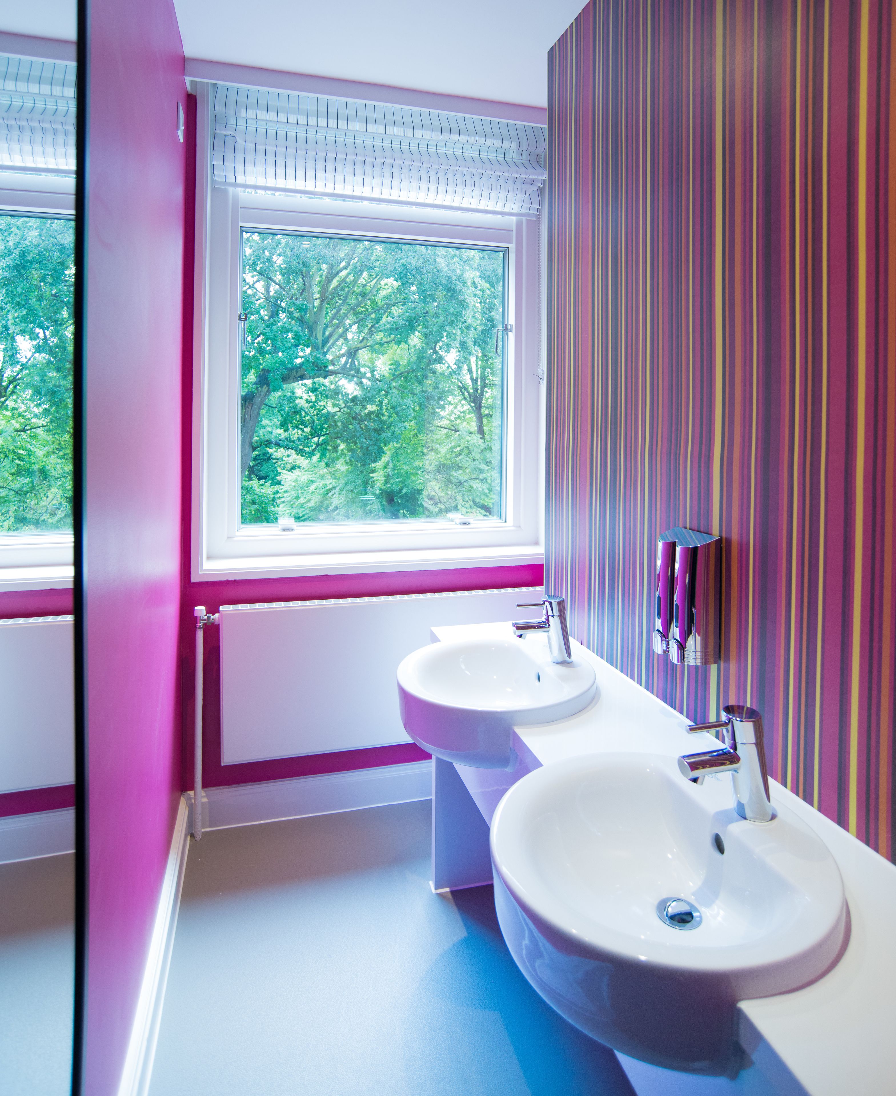 Une salle de bain avec deux lavabos, une fenêtre et un mur à rayures.