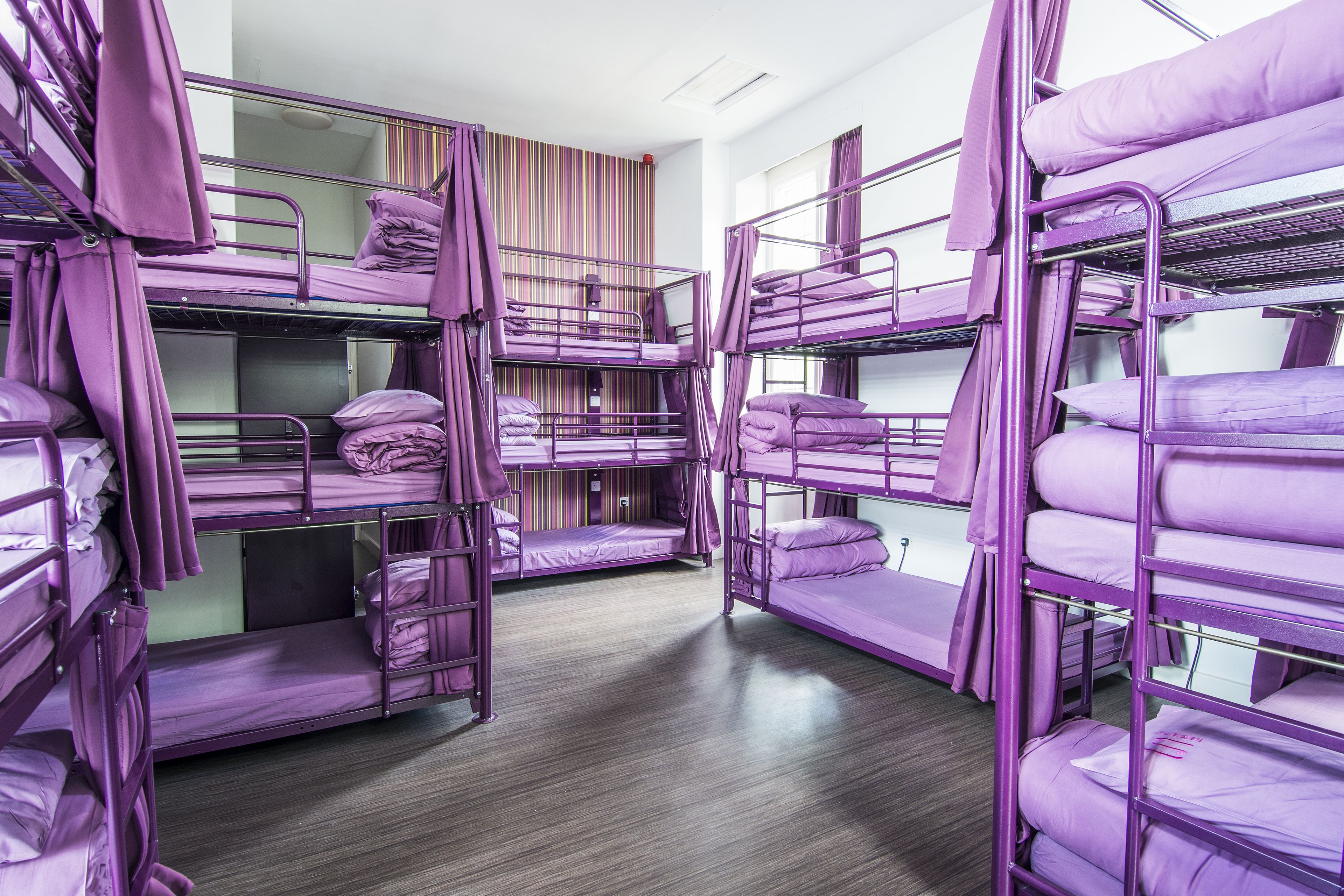A room with bunk beds, wooden flooring, and a striped curtain.
