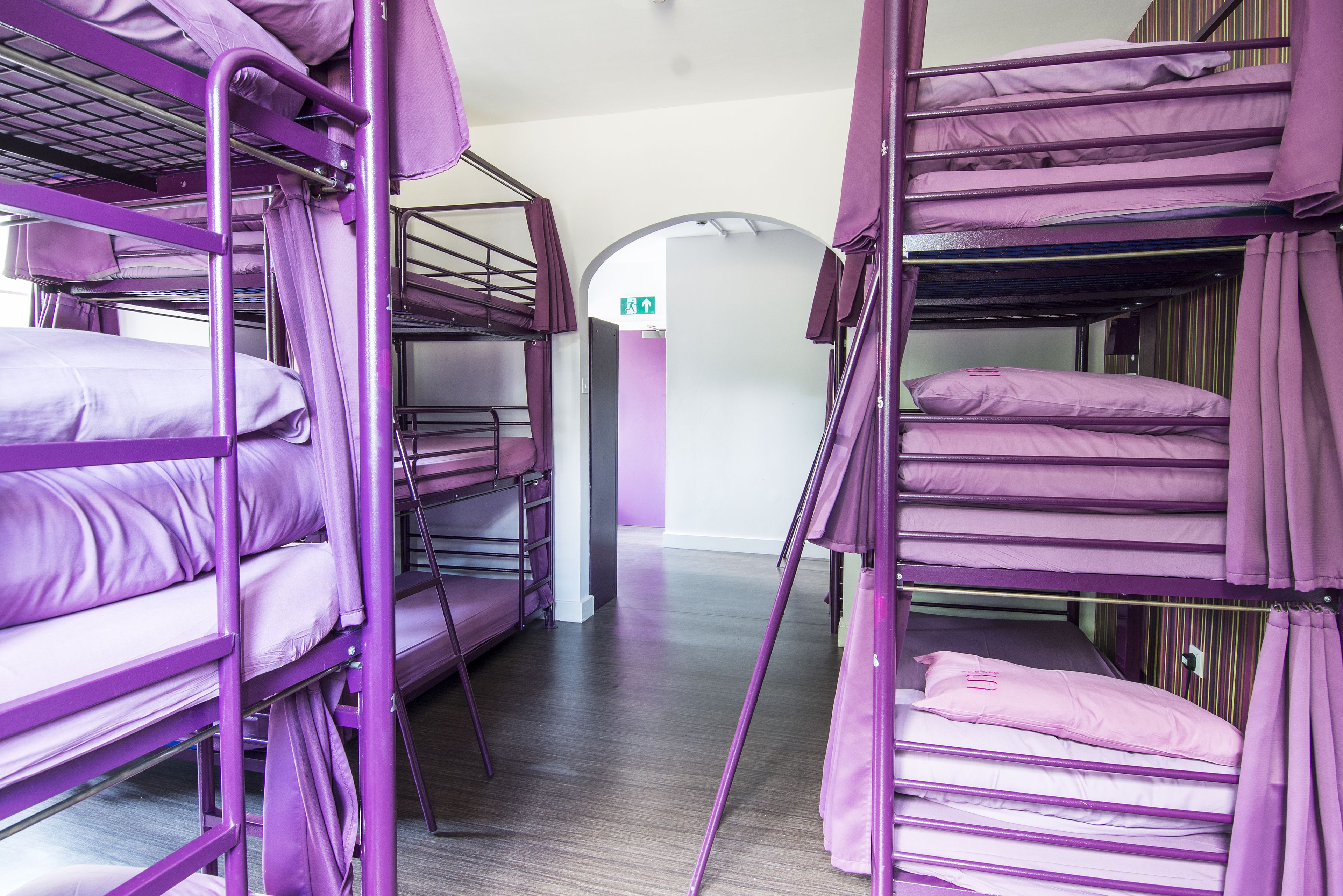A room with bunk beds, a wooden floor, and a door with an emergency exit sign.