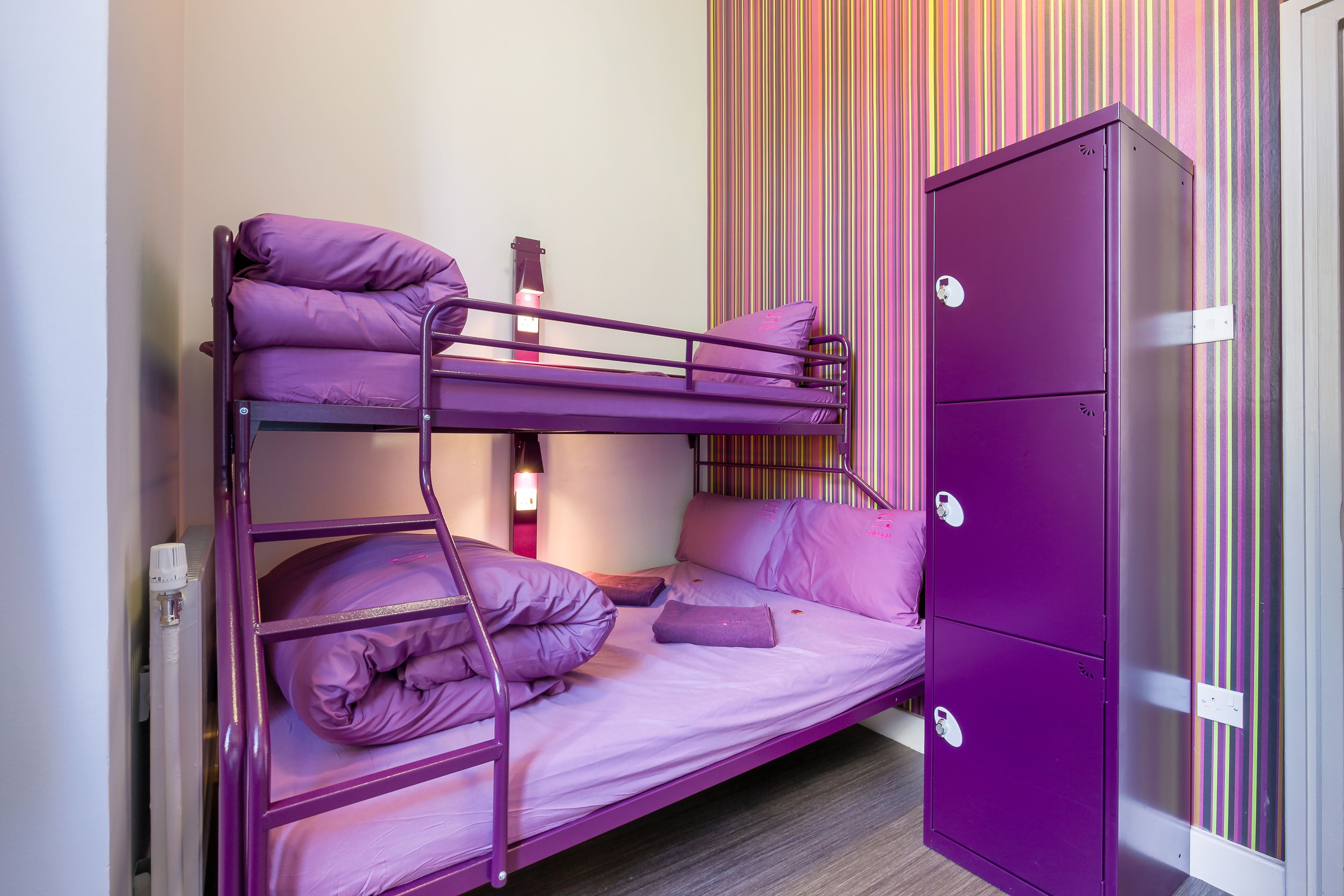 Una cama litera con ropa de cama morada y un armario de dos puertas.