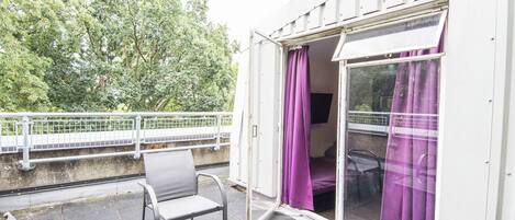 A balcony with a table and chairs, a purple curtain, and a view of trees.