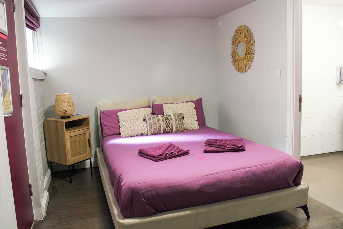 A bedroom with a bed, pillows, a bedside table, and a wall decoration.