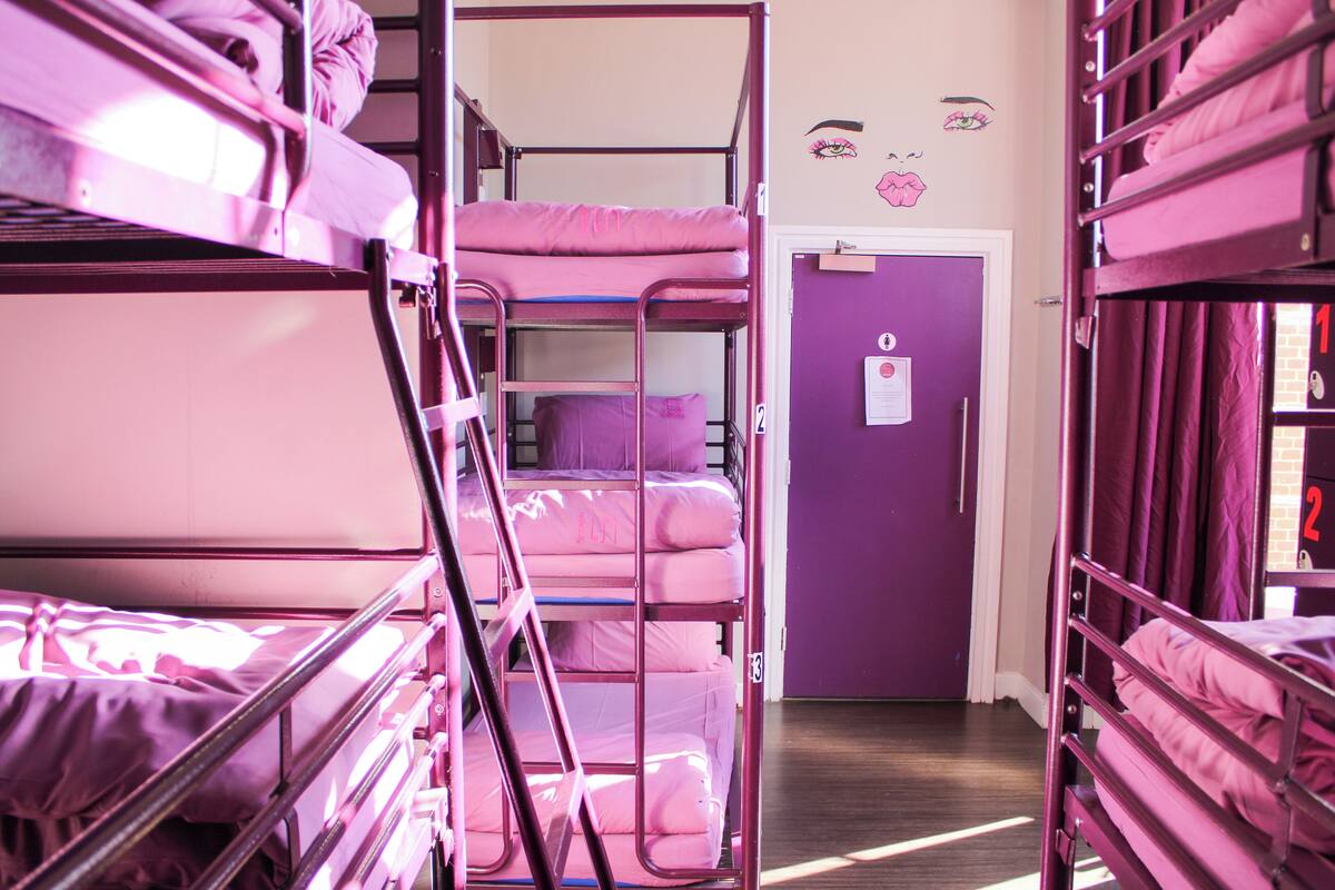 Bunk beds with pink bedding in a room with purple walls and a door with a number sign.