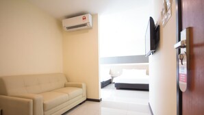 A hotel room with a beige sofa, a bed, a flat-screen TV mounted on the wall, and an air conditioning unit on the ceiling. - 118 Hotel Macalister (George Town)