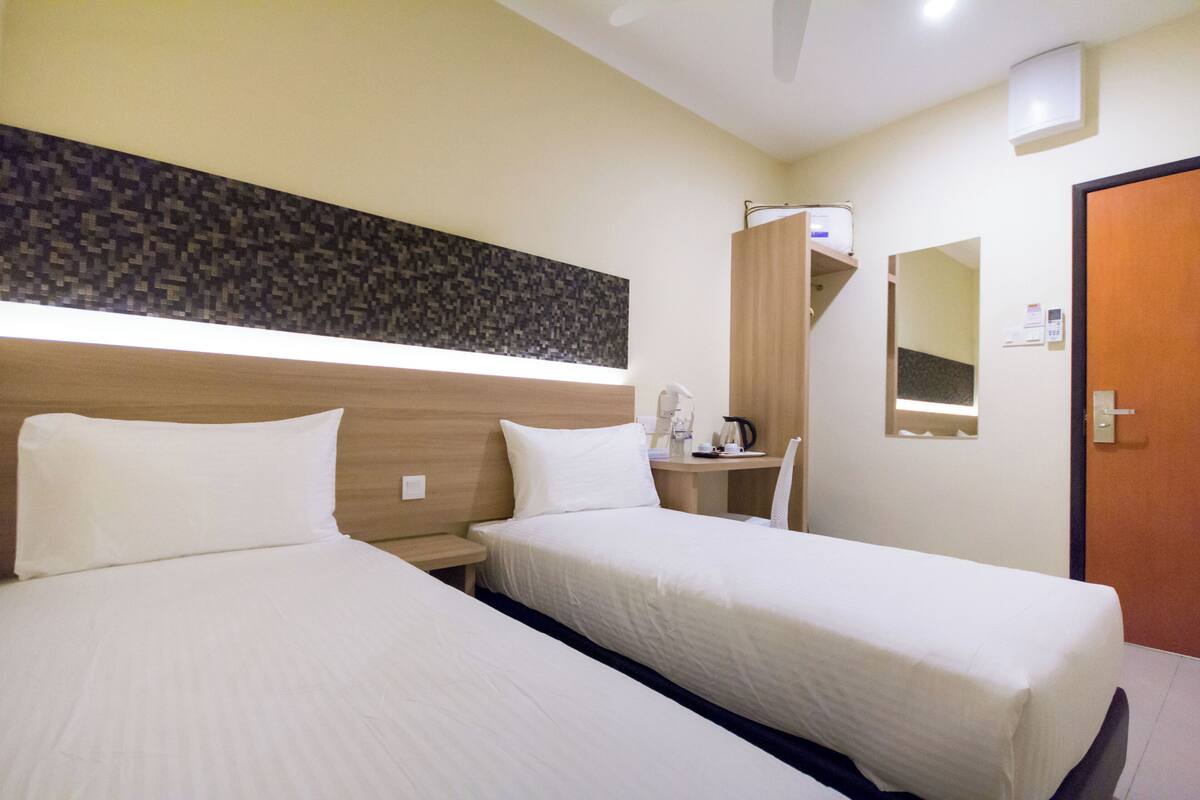 A hotel room with two beds, a small desk, a mirror, and a door.