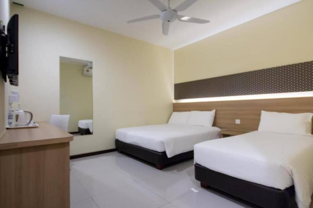 A hotel room with two beds, a desk, a ceiling fan, and a mirror.