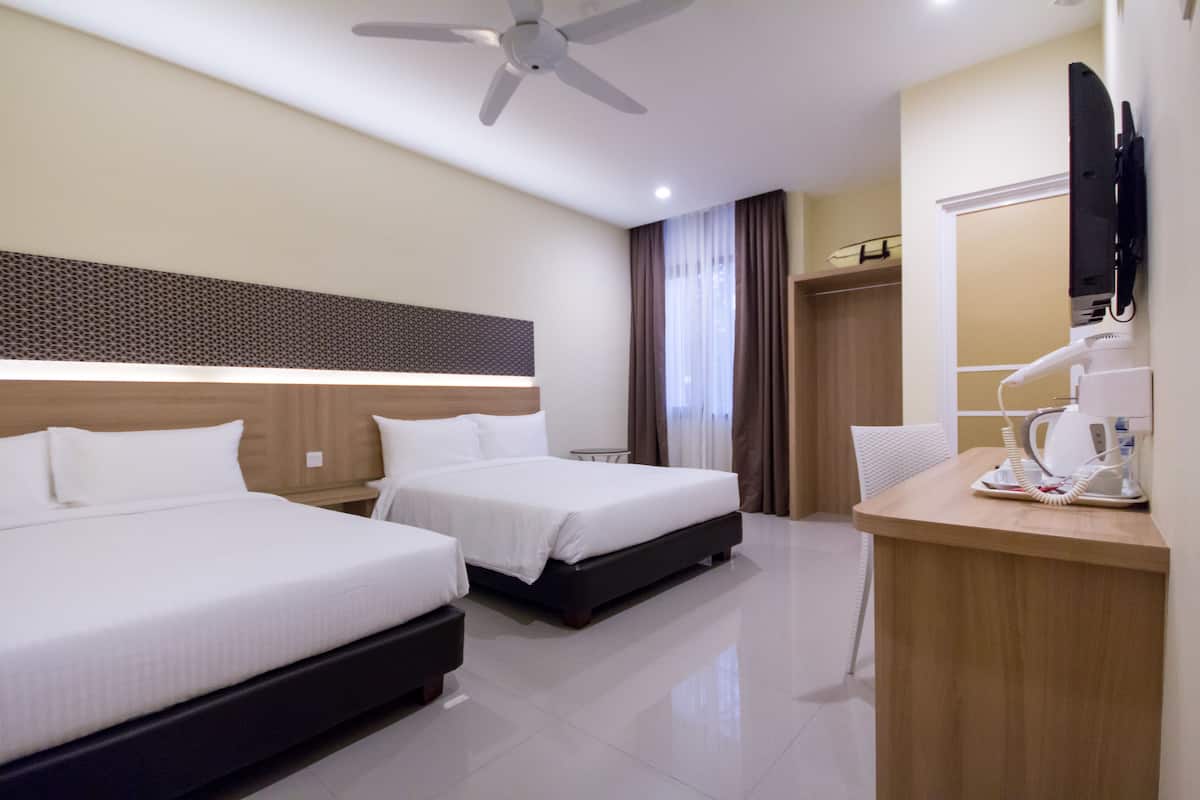A hotel room with two beds, a desk with a lamp, a ceiling fan, and a TV mounted on the wall.