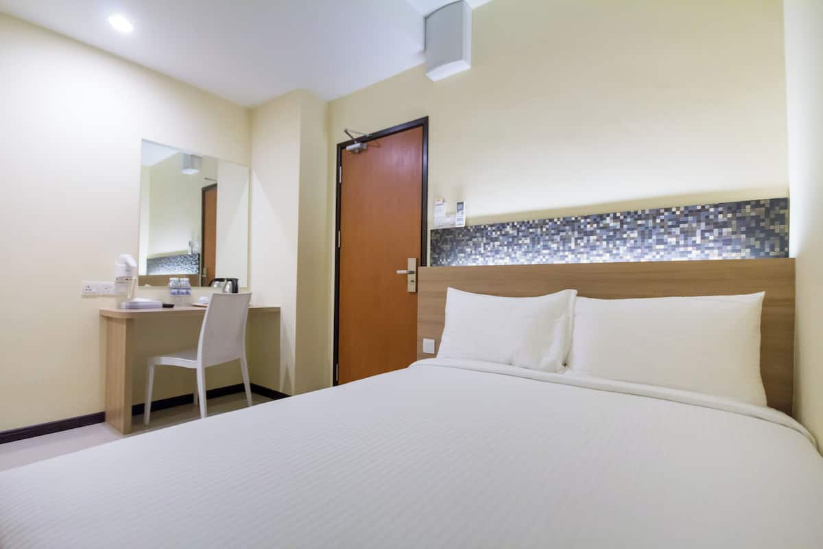 A hotel room with a bed, a desk, a chair, a mirror, and a door.