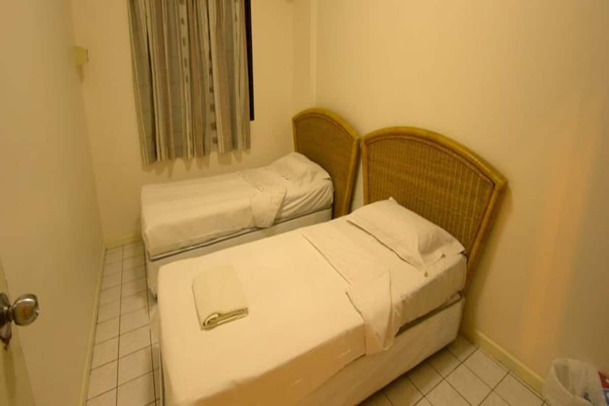 A small, single-room hotel room with two single beds, a window with curtains, and a tiled floor.