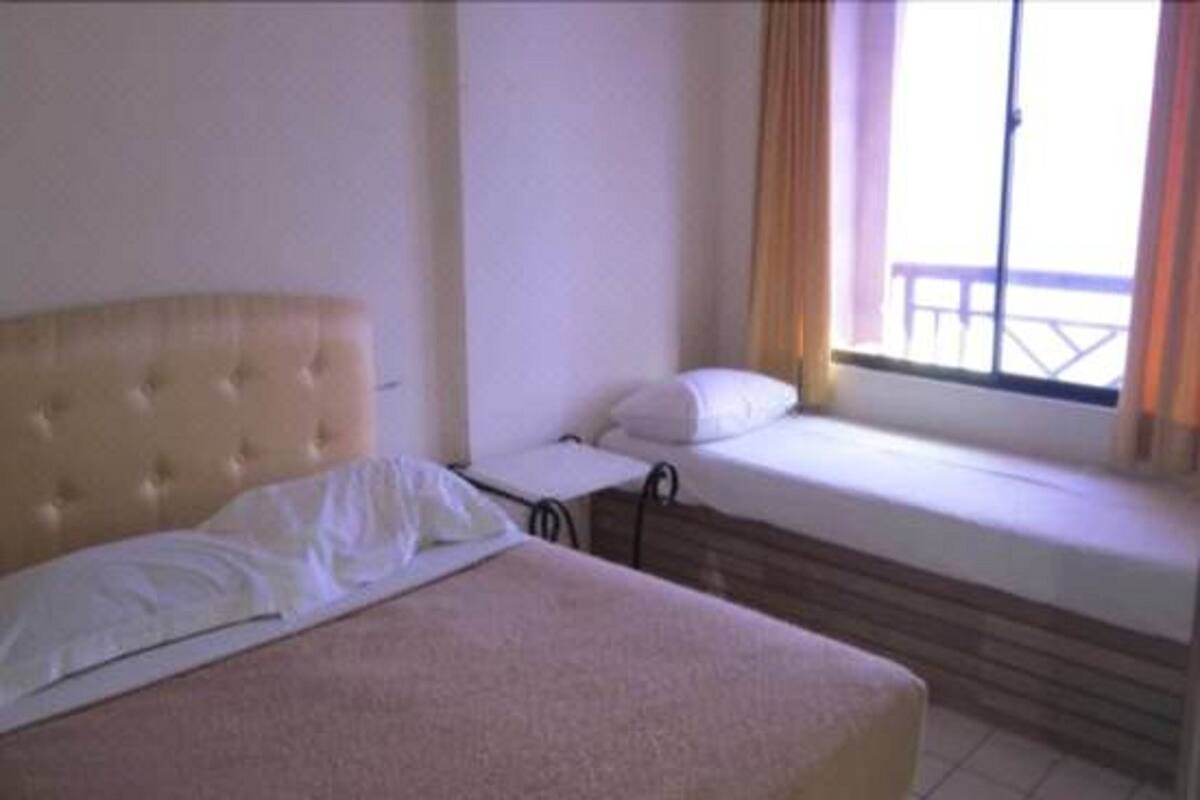 A room with a large bed, a smaller bed, and a window with curtains.