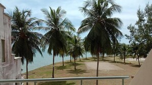 A balcony with a view of palm trees and a beach. - Paradise Lagoon Apartment (Port Dickson)