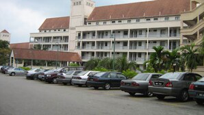 A multi-story hotel with a central tower, parking lot, and several cars parked in front. - Paradise Lagoon Apartment (Port Dickson)
