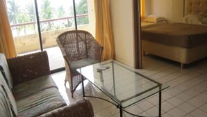 A room with a glass-top table, wicker sofa, and a bed. - Paradise Lagoon Apartment (Port Dickson)