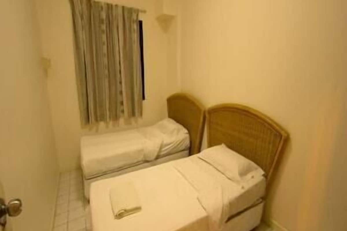 A small, single-bed room with a wooden headboard, a window with curtains, and a tiled floor.