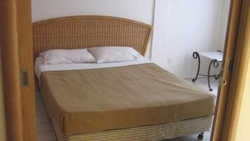 A single bed with a striped mattress, a beige bedspread, and white pillows.